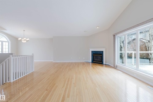 Expansive room featuring light hardwood flooring, a fireplace with a blue tile surround, large windows, and a vaulted ceiling - 1641 Forbes Way, Edmonton, AB - Indoor With Fireplace