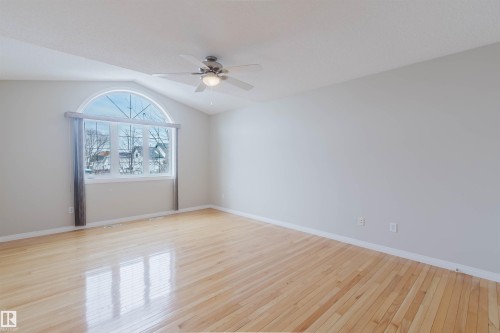 This room features polished hardwood flooring, a vaulted ceiling, and an arched window providing ample natural light - 1641 Forbes Way, Edmonton, AB - Indoor Photo Showing Other Room