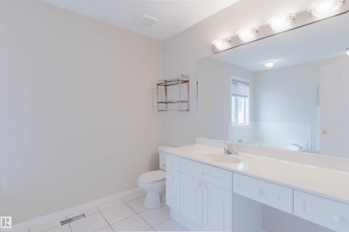 Bathroom featuring a white vanity with an integrated sink, a rectangular mirror with overhead lighting, a toilet, and white floor tiles - 1641 Forbes Way, Edmonton, AB - Indoor Photo Showing Bathroom