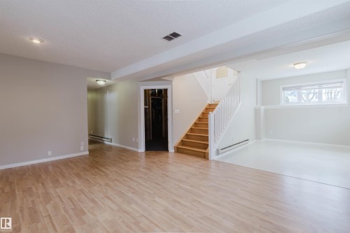 Spacious interior featuring light wood flooring, a white staircase with wood treads, and white walls - 1641 Forbes Way, Edmonton, AB - Indoor Photo Showing Other Room