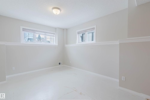 This room features neutral-toned walls with white trim, two windows providing natural light, and a ceiling-mounted light fixture - 1641 Forbes Way, Edmonton, AB - Indoor Photo Showing Other Room