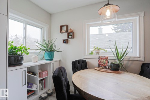 Dining area with a light wood oval table and two dark upholstered chairs - 9319 92 Street, Edmonton, AB - Indoor Photo Showing Dining Room