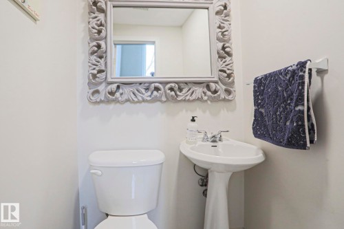 The bathroom features a white pedestal sink with a chrome faucet, a white toilet, and a decorative framed mirror - 9319 92 Street, Edmonton, AB - Indoor Photo Showing Bathroom