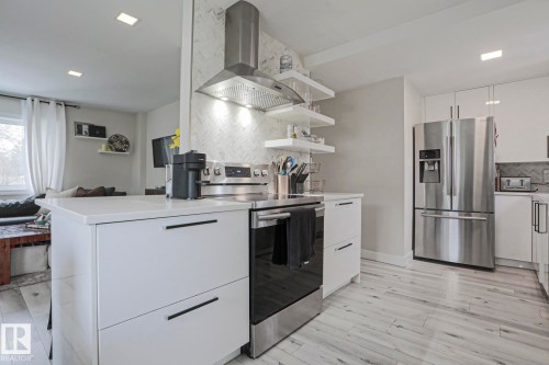 The kitchen features white cabinetry with dark hardware, stainless steel appliances including a refrigerator and range, and light-toned flooring - 9319 92 Street, Edmonton, AB - Indoor Photo Showing Kitchen With Stainless Steel Kitchen