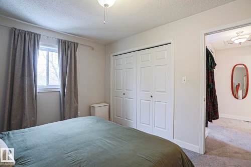 This room features a window with curtains, a ceiling light fixture, and a white bi-fold closet - 9319 92 Street, Edmonton, AB - Indoor Photo Showing Bedroom