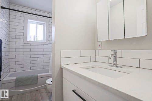 Bathroom featuring a white subway tiled shower and tub combination, a window providing natural light, a vanity with a white countertop, and a mirrored medicine cabinet - 9319 92 Street, Edmonton, AB - Indoor Photo Showing Bathroom