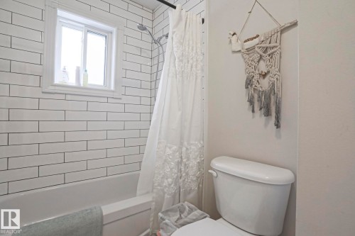The bathroom features a white subway-tiled shower and bath combination with a window providing natural light - 9319 92 Street, Edmonton, AB - Indoor Photo Showing Bathroom