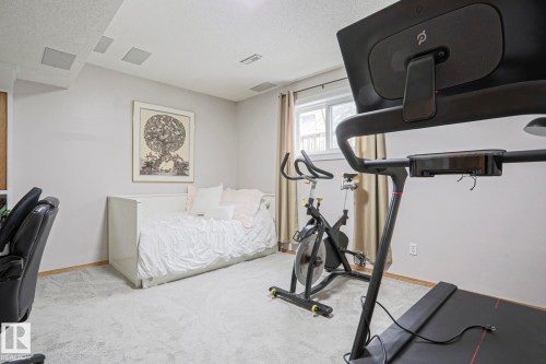 This versatile room features light-colored walls, carpeted flooring, and a window with curtains - 9319 92 Street, Edmonton, AB - Indoor Photo Showing Gym Room