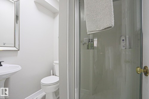 Bathroom featuring a pedestal sink, a toilet, a shower with a glass enclosure, and a decorative mirror - 9319 92 Street, Edmonton, AB - Indoor Photo Showing Bathroom