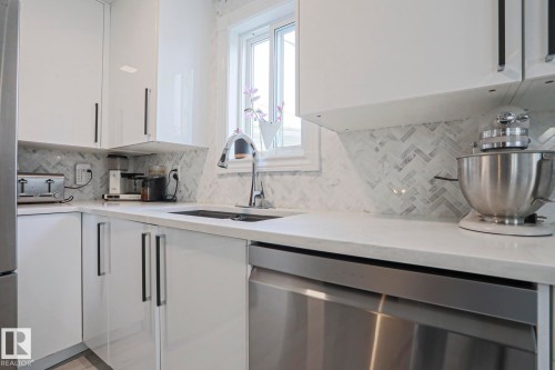 The kitchen features white cabinetry with modern handles, a grey herringbone tile backsplash, and light-colored countertops - 9319 92 Street, Edmonton, AB - Indoor Photo Showing Kitchen