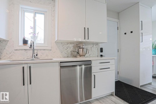 The kitchen features sleek white cabinetry with dark hardware, a stainless steel dishwasher, and a white countertop - 9319 92 Street, Edmonton, AB - Indoor Photo Showing Kitchen With Upgraded Kitchen