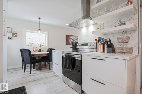 The kitchen features white cabinetry with black hardware, stainless steel appliances, and a herringbone pattern tile backsplash - 9319 92 Street, Edmonton, AB - Indoor