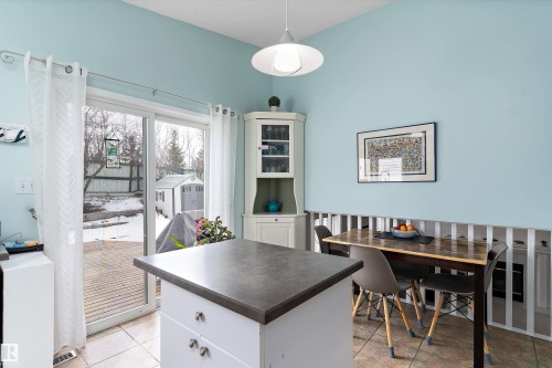 The kitchen features a functional island with a dark countertop and white cabinetry, tile flooring, and light blue walls - 322 Pearson Crescent, Edmonton, AB - Indoor Photo Showing Dining Room