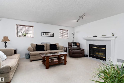The living area features light-colored carpeting, white walls, and a fireplace with a white mantel and black surround - 322 Pearson Crescent, Edmonton, AB - Indoor Photo Showing Living Room With Fireplace