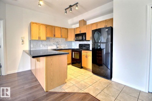 The kitchen features light wood cabinetry, black appliances, and a black countertop on the island - 209 10235 112 Street, Edmonton, AB - Indoor Photo Showing Kitchen