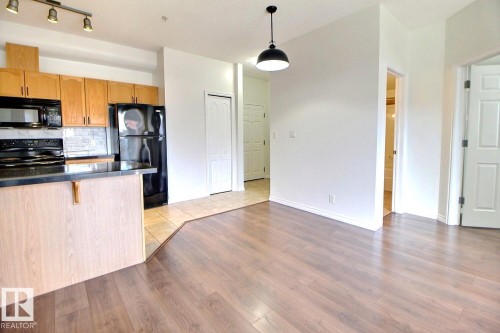 The kitchen features light wood cabinetry, black appliances, and a tiled backsplash - 209 10235 112 Street, Edmonton, AB - Indoor Photo Showing Kitchen