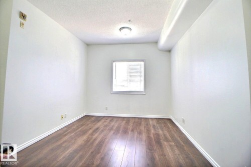 This room features hardwood style flooring, white walls, and a window providing natural light - 209 10235 112 Street, Edmonton, AB - Indoor Photo Showing Other Room