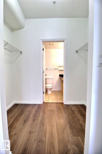 Well-maintained space featuring wood-look flooring and white walls, with an open doorway leading to a tiled area with a toilet - 209 10235 112 Street, Edmonton, AB - Indoor