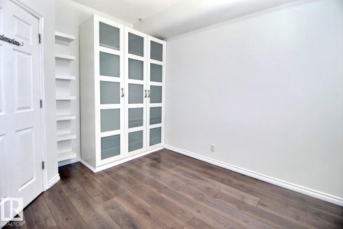 This room features wood-look flooring, white walls, and a built-in wardrobe with frosted glass panels - 209 10235 112 Street, Edmonton, AB - Indoor Photo Showing Other Room