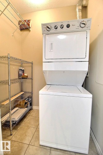 The property includes a laundry area with a stacked washer and dryer unit, tiled flooring, and a wire shelving unit for storage - 209 10235 112 Street, Edmonton, AB - Indoor Photo Showing Laundry Room