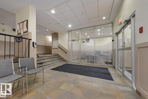This space features tile flooring, paneling on the walls, and a staircase with a black handrail - 209 10235 112 Street, Edmonton, AB - Indoor Photo Showing Other Room