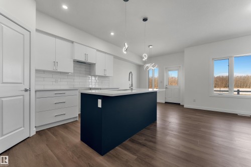 The property features an open-concept living space with dark wood flooring, white walls, and recessed lighting - 114 Mitchell Bend, Leduc, AB - Indoor Photo Showing Kitchen With Upgraded Kitchen