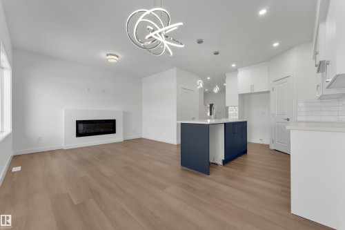 Open concept living area featuring light wood flooring, a fireplace, and a modern chandelier - 114 Mitchell Bend, Leduc, AB - Indoor With Fireplace