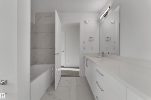 Contemporary bathroom featuring a white vanity with integrated sink, a bathtub with tiled surround, and a large wall-mounted mirror - 114 Mitchell Bend, Leduc, AB - Indoor Photo Showing Bathroom