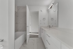 Contemporary bathroom featuring a white vanity with integrated sink, a bathtub with tiled surround, and a large wall-mounted mirror - 