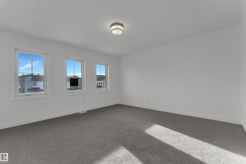 This room features three windows providing natural light, a ceiling-mounted light fixture, and grey carpet flooring - 114 Mitchell Bend, Leduc, AB - Indoor Photo Showing Other Room