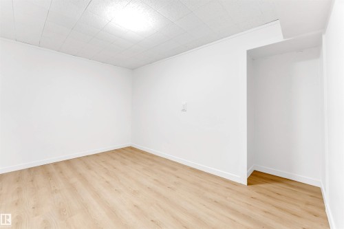 This versatile room features light-toned wood-style flooring, white walls, and a white grid-patterned ceiling with an overhead light fixture - 12423 91 Street, Edmonton, AB - Indoor Photo Showing Other Room