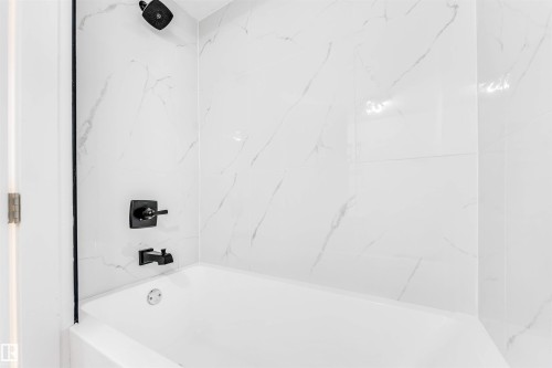 Bathtub with white marble-patterned tile surround and matte black fixtures - 12423 91 Street, Edmonton, AB - Indoor Photo Showing Bathroom