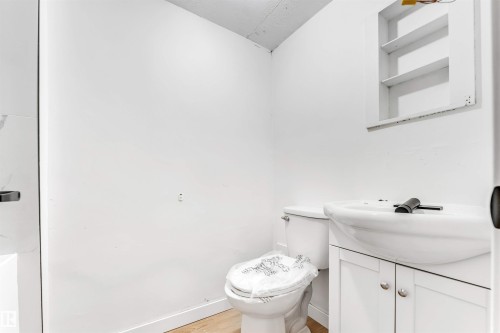 This bathroom features a white vanity with cabinet storage, a white toilet, and a wall-mounted shelving unit - 12423 91 Street, Edmonton, AB - Indoor Photo Showing Bathroom