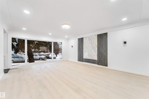 Spacious living area featuring light-toned flooring, recessed lighting, and a decorative wall panel with intricate detailing - 12423 91 Street, Edmonton, AB - Indoor