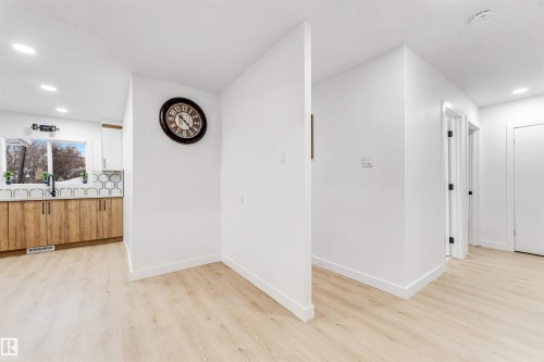 This property features light-toned flooring, white walls, and a kitchen with wooden lower cabinets, white upper cabinets, a window, and a white and grey patterned backsplash - 12423 91 Street, Edmonton, AB - Indoor Photo Showing Other Room