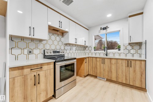 The kitchen features white upper cabinetry, natural wood tone lower cabinetry, a patterned backsplash, and a window above the sink - 12423 91 Street, Edmonton, AB - Indoor Photo Showing Kitchen