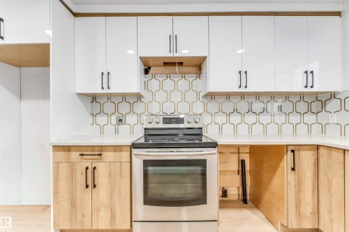The kitchen features a modern aesthetic with white upper cabinetry and light wood lower cabinetry, complemented by a white countertop - 12423 91 Street, Edmonton, AB - Indoor Photo Showing Kitchen