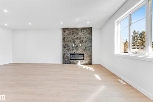 Bright living area featuring a contemporary fireplace with a textured stone surround, light-colored wood flooring, and large windows - 10962 157 Street, Edmonton, AB - Indoor With Fireplace