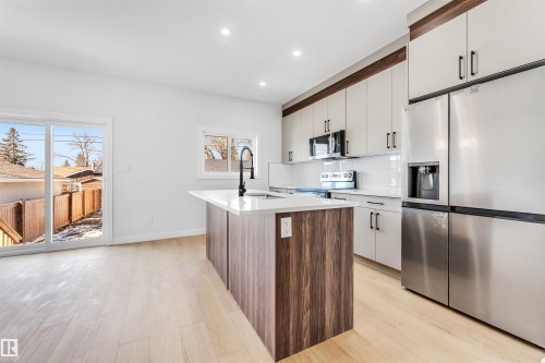 Modern kitchen featuring light-toned cabinetry, stainless steel appliances, a kitchen island with a white countertop and dark wood paneling, and light wood flooring - 10962 157 Street, Edmonton, AB - Indoor Photo Showing Kitchen With Upgraded Kitchen