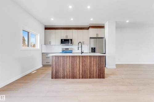 The kitchen features a large island with a wood-look base, a white countertop, and a black faucet - 10962 157 Street, Edmonton, AB - Indoor Photo Showing Kitchen