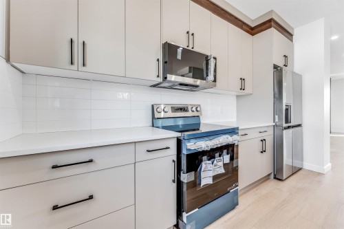 The kitchen features light-toned cabinetry with dark hardware, white countertops, a subway tile backsplash, and stainless steel appliances including a range, microwave, and refrigerator - 10962 157 Street, Edmonton, AB - Indoor Photo Showing Kitchen With Upgraded Kitchen