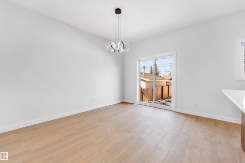 This bright space features light-colored flooring, a contemporary chandelier, and sliding glass doors that provide access to the outdoors - 10962 157 Street, Edmonton, AB - Indoor Photo Showing Other Room