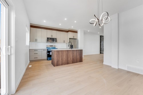 The open-concept kitchen features a central island, stainless steel appliances, and a tiled backsplash - 10962 157 Street, Edmonton, AB - Indoor Photo Showing Kitchen