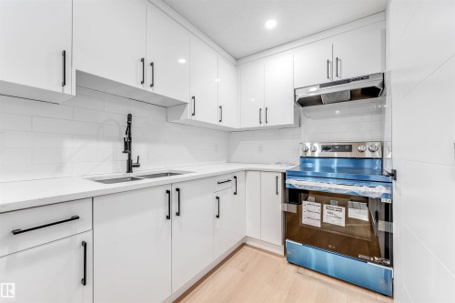 The kitchen features white cabinetry with black hardware, a stainless steel range with a range hood, and a dual basin sink with a black faucet - 10962 157 Street, Edmonton, AB - Indoor Photo Showing Kitchen With Double Sink