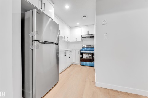The kitchen features bright white cabinetry, stainless steel appliances including a refrigerator and range, a light-colored countertop, and light hardwood flooring - 10962 157 Street, Edmonton, AB - Indoor Photo Showing Kitchen