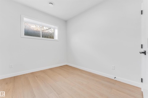 This room features light-toned hardwood flooring, a white trim window, and white walls - 10962 157 Street, Edmonton, AB - Indoor Photo Showing Other Room