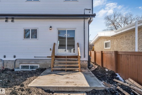 Rear exterior of the property featuring white siding, a sliding glass door, and a concrete patio with wooden steps - 10962 157 Street, Edmonton, AB - Outdoor With Exterior