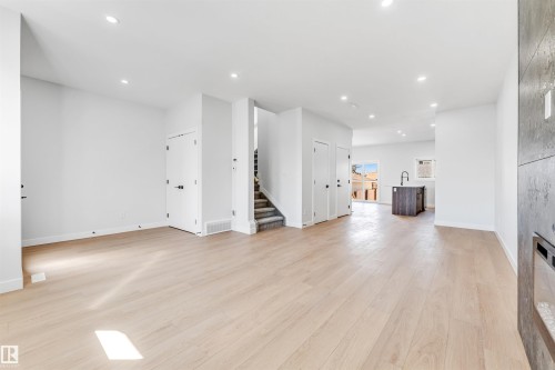 Spacious open concept interior with light-colored flooring, recessed lighting, and a dark-colored kitchen island featuring a sink - 10962 157 Street, Edmonton, AB - Indoor