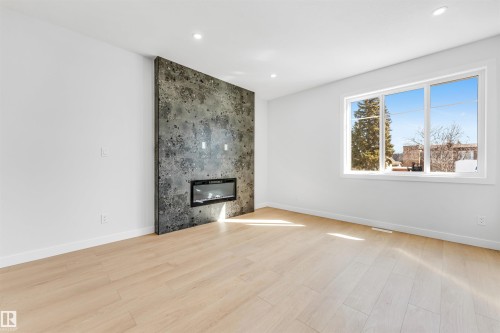 Spacious living area featuring light-toned flooring, an accent wall with a modern fireplace, and large windows providing natural light - 10962 157 Street, Edmonton, AB - Indoor Photo Showing Living Room With Fireplace