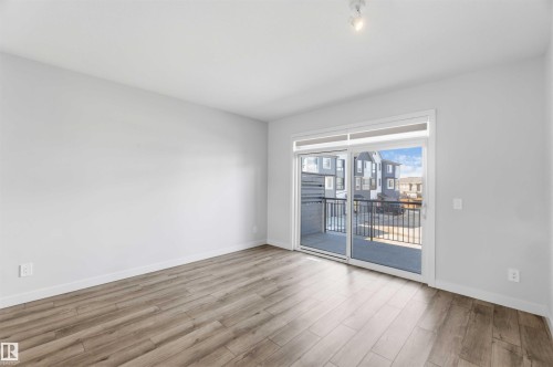 The property features light-toned walls, wood-style flooring, and a sliding glass door providing balcony access - 49 100 Jensen Lakes Boulevard, St. Albert, AB - Indoor Photo Showing Other Room